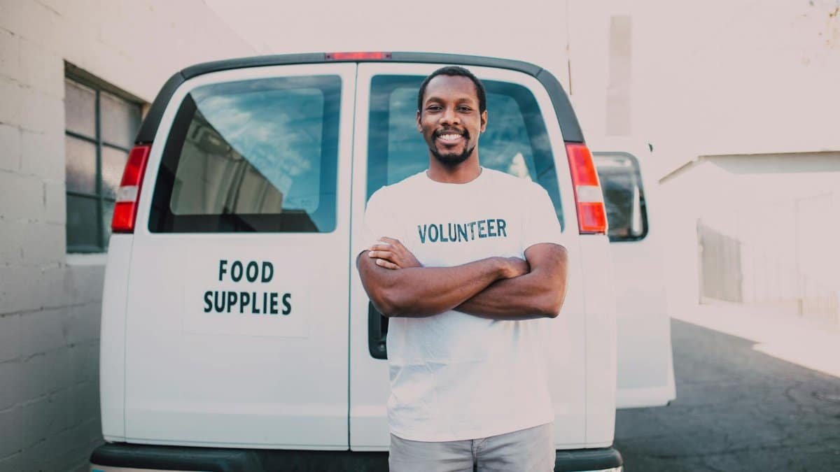Male volunteer standing confidently in front of a food delivery van.