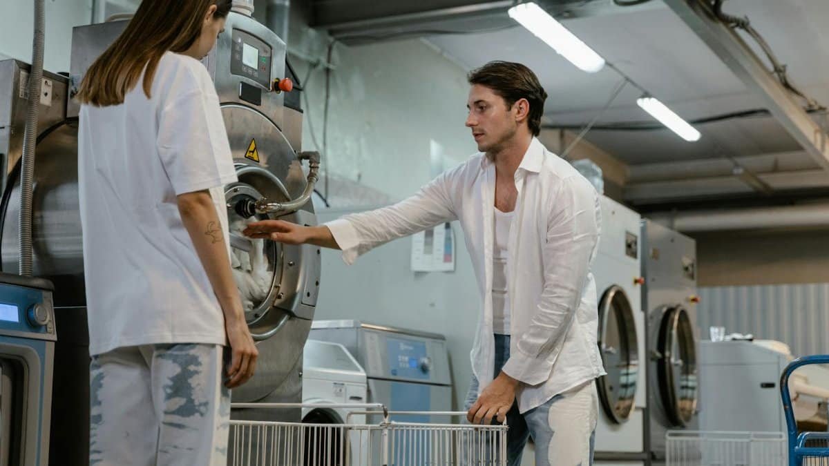 Two adults operating industrial laundry machines in a modern facility, showcasing teamwork and technology.