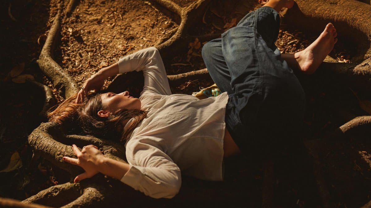 Woman lying on tree roots outdoors, basking in warm sunlight, peaceful setting.