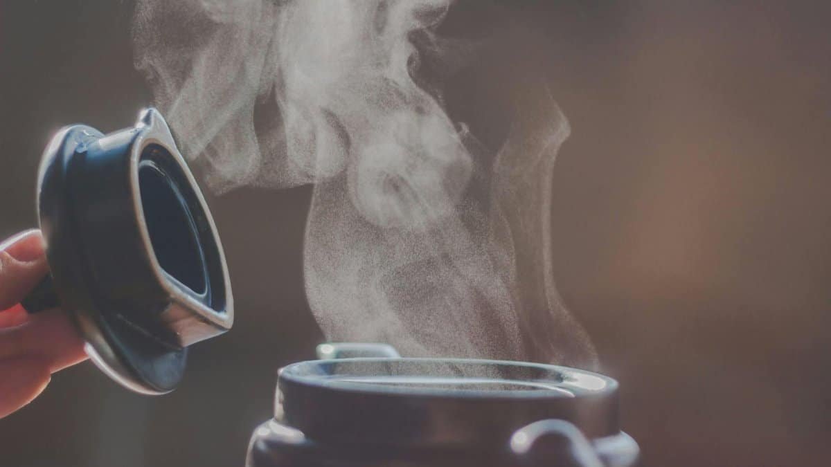 Close-up of steam rising from an open container lid showing hot liquid.
