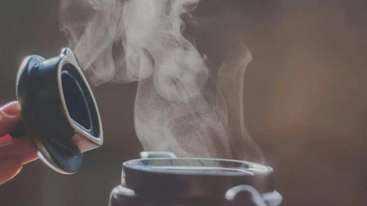 Close-up of steam rising from an open container lid showing hot liquid.