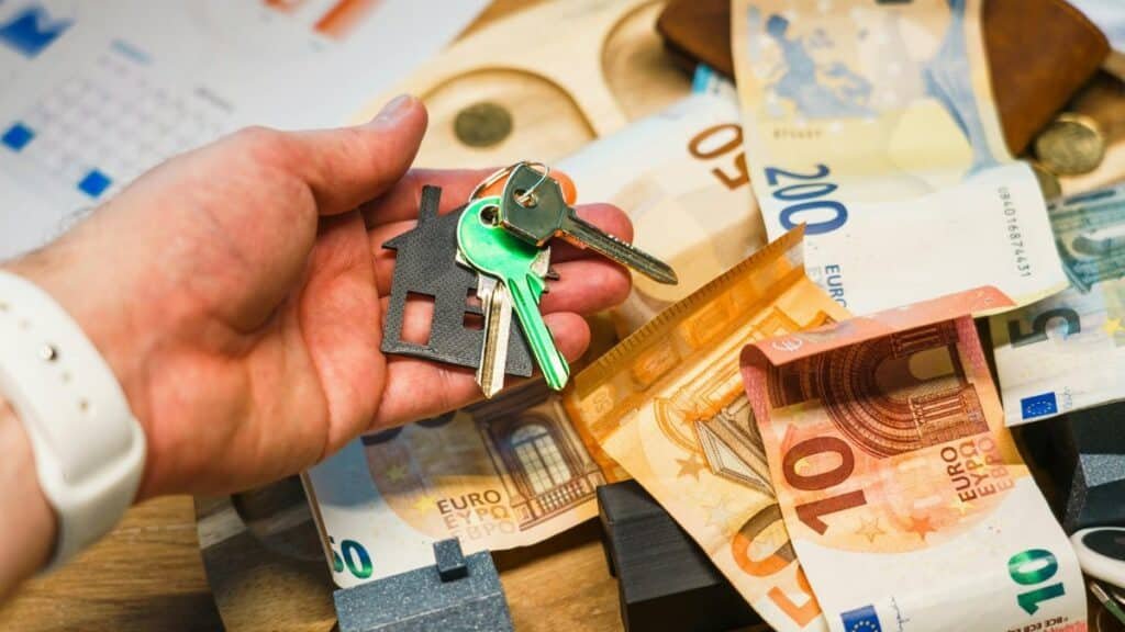 A hand holding house keys over euro banknotes, symbolizing real estate and finance.