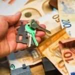 A hand holding house keys over euro banknotes, symbolizing real estate and finance.