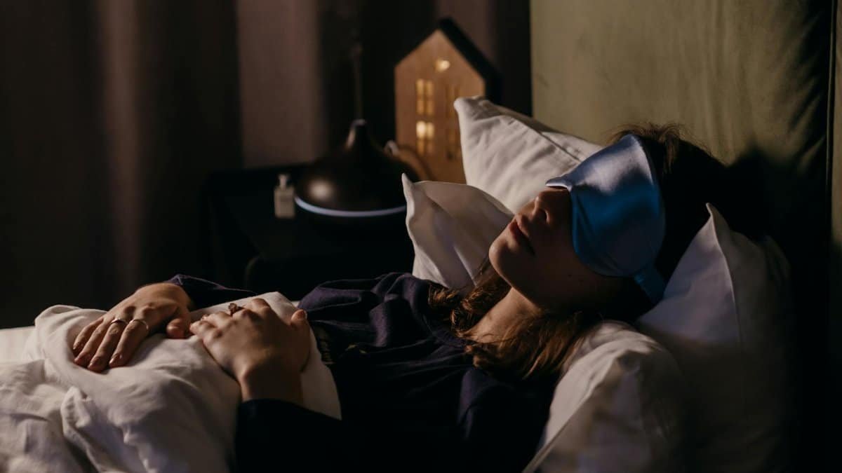 A woman resting with a sleep mask in a calm bedroom setting, creating a serene and cozy atmosphere.