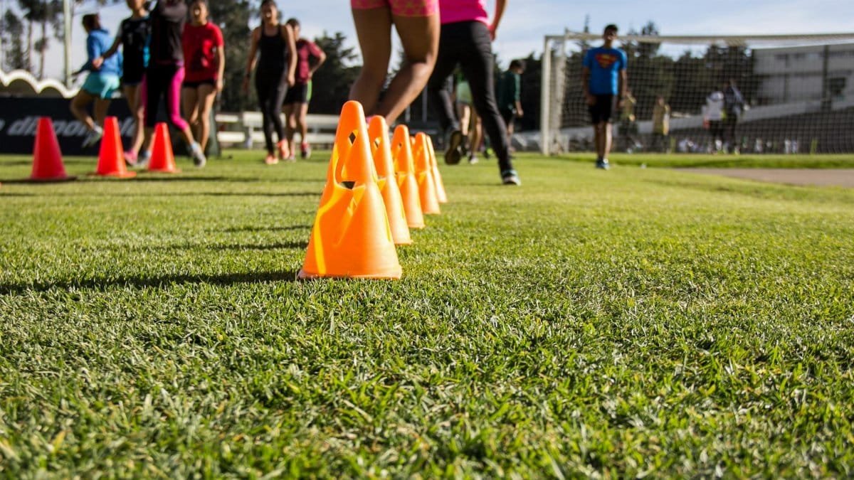 Dynamic soccer training session with teenagers practicing agility using orange cones on grass field.