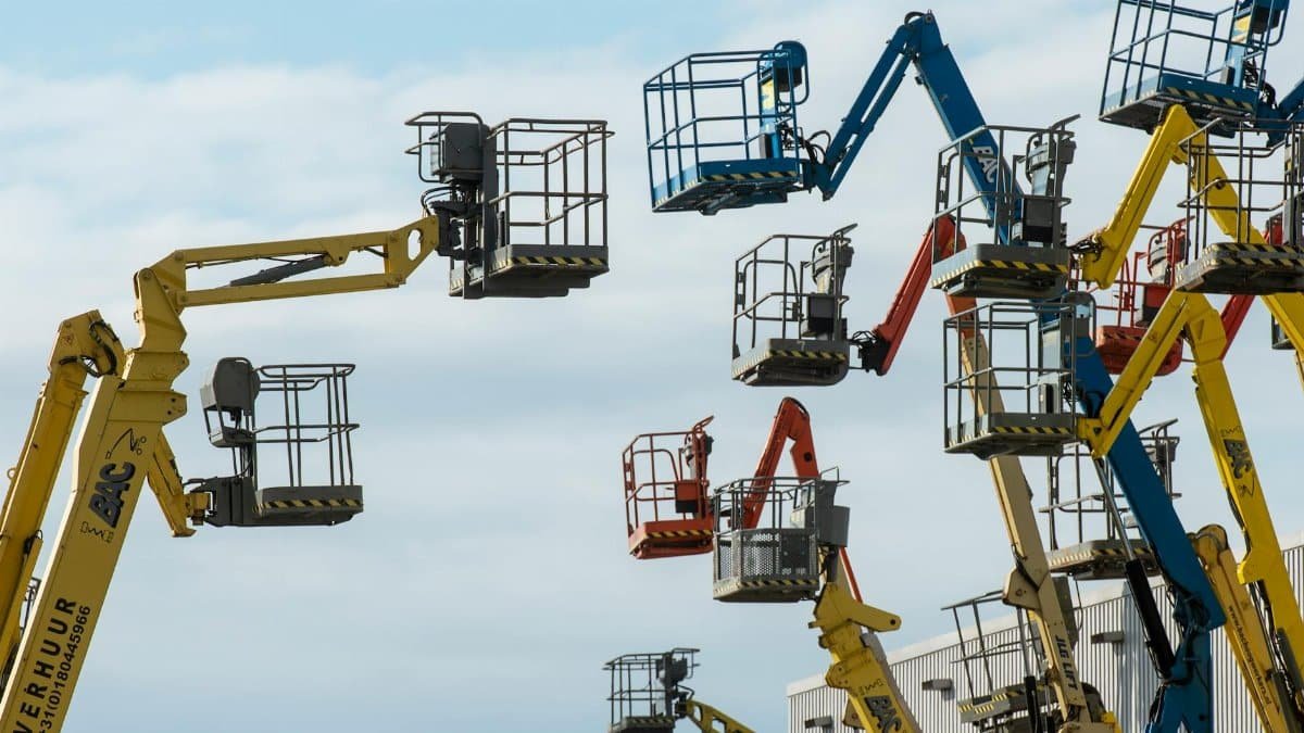 A collection of colorful boom lifts reaching toward a clear blue sky, showcasing industrial machinery.