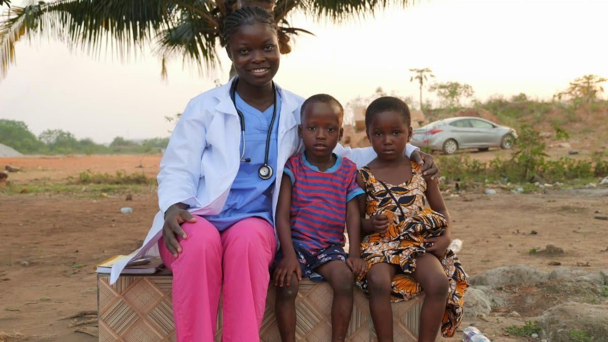 Female healthcare worker smiles with two children outside, showcasing community care.