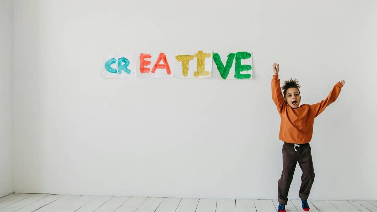 Young boy jumps joyfully in front of colorful 'creative' text on the wall.