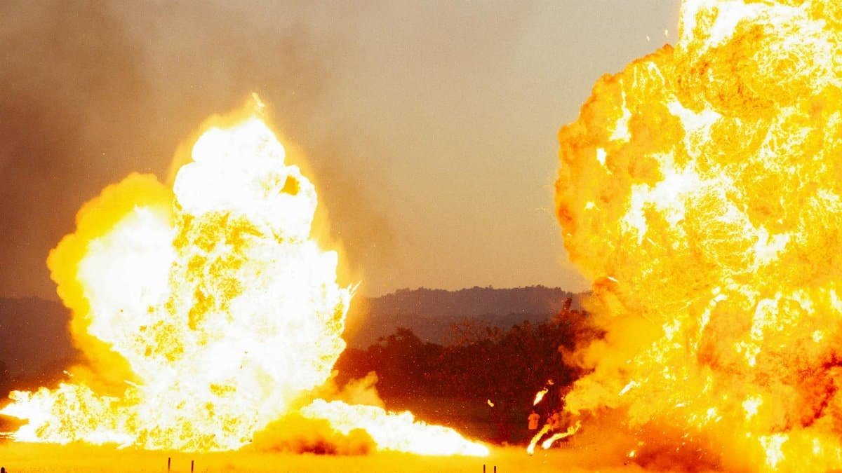 Powerful explosion with bright flames against an outdoor landscape, creating a dramatic visual impact.