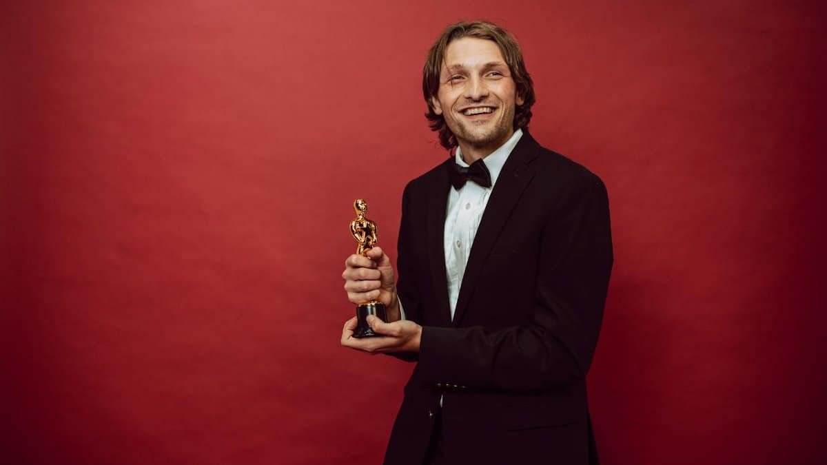 Portrait of a happy man in a suit holding a trophy on a red backdrop, celebrating success.
