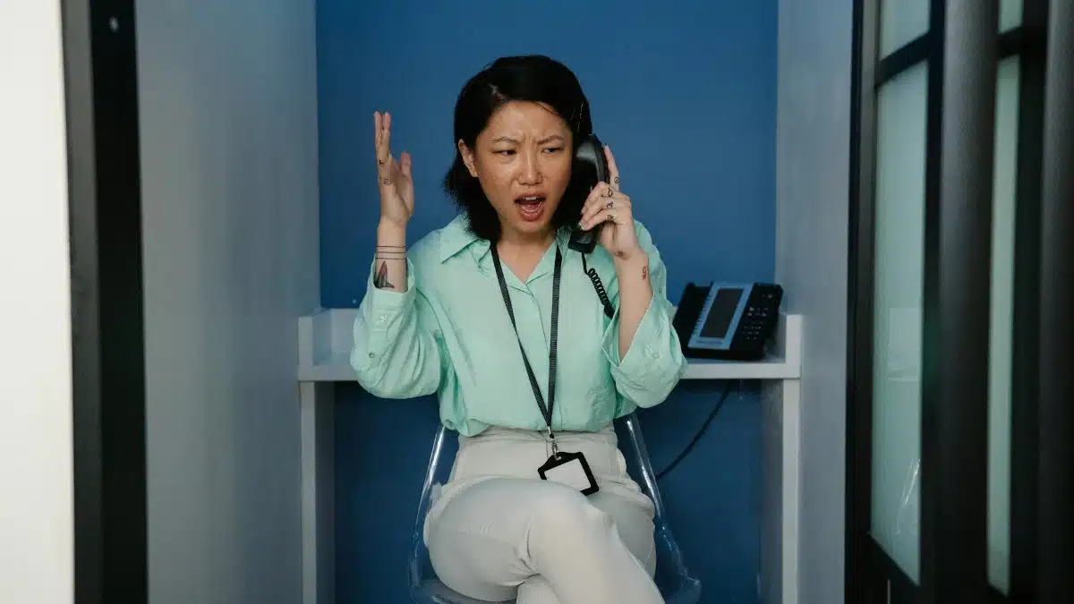 An east Asian woman expressing frustration during a phone call at the workplace.