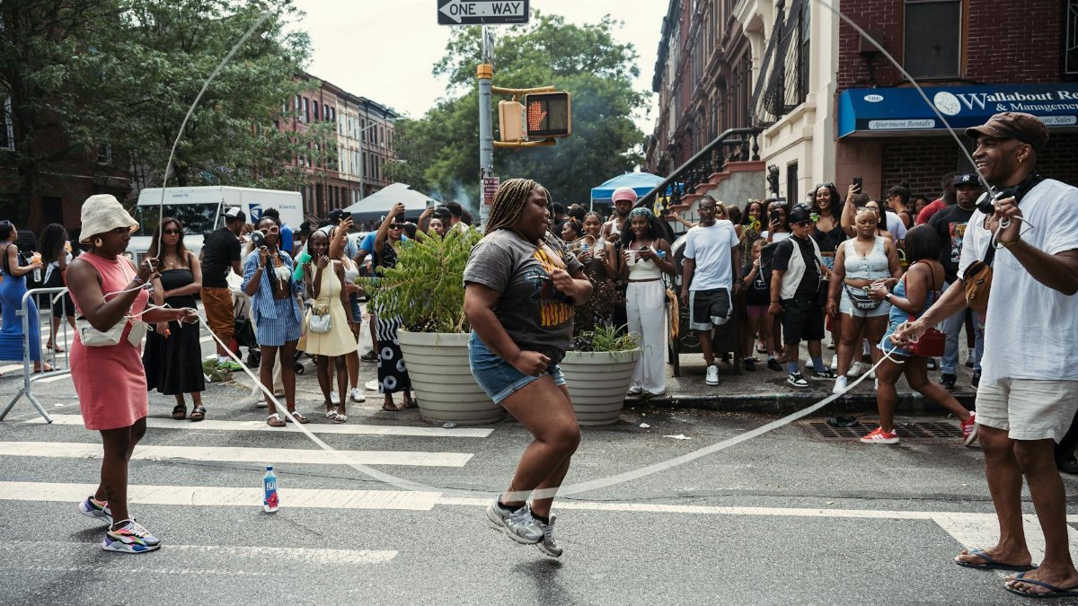 Joyful scene at a lively Brooklyn block party with people enjoying jump rope and street festivities.