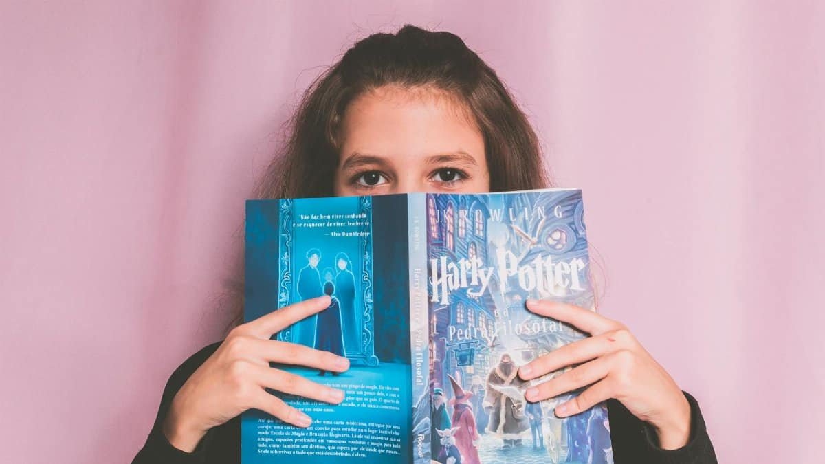 A young girl poses with a Harry Potter book against a pink backdrop, capturing a candid reading moment.