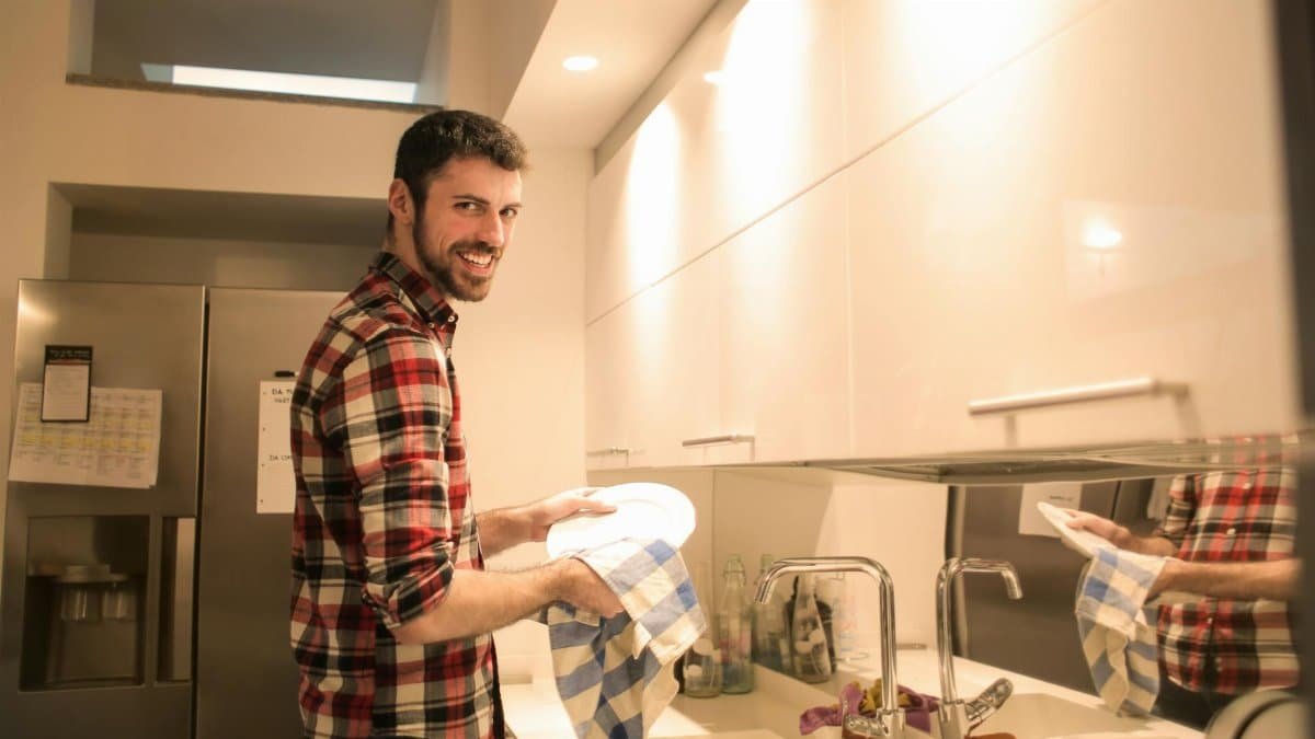 A cheerful man cleans dishes in a bright, contemporary kitchen setting.