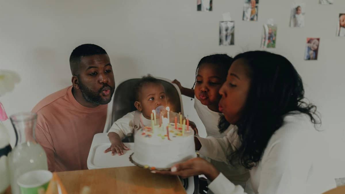 A joyful family celebrating a baby's first birthday with cake and candles indoors.