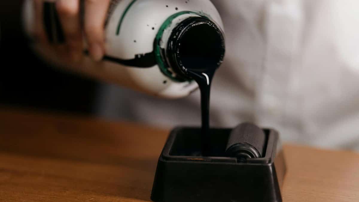 A close-up image of ink from a bottle being poured onto a roller, highlighting art supplies.
