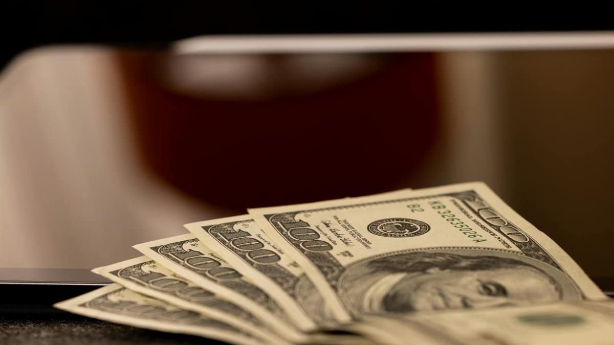 Close-up image of multiple dollar bills placed beside a laptop, symbolizing finance and digital economy.