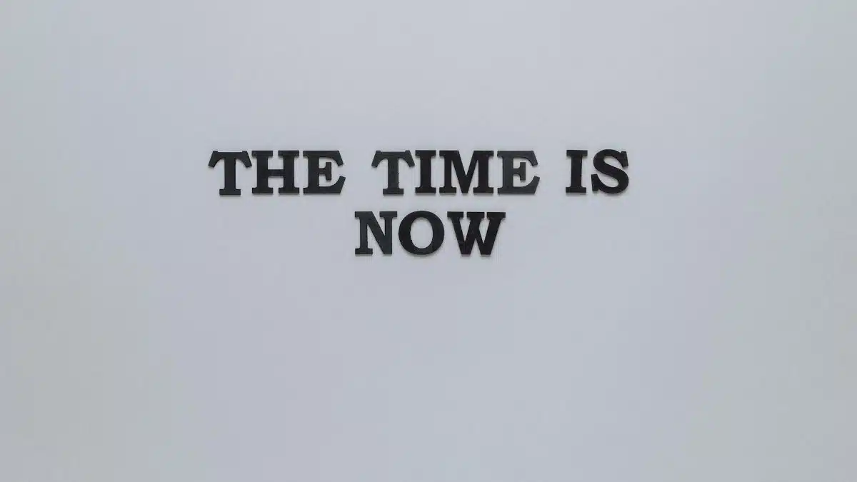 Minimalist poster with the motivational quote 'The Time is Now' on a gray background.