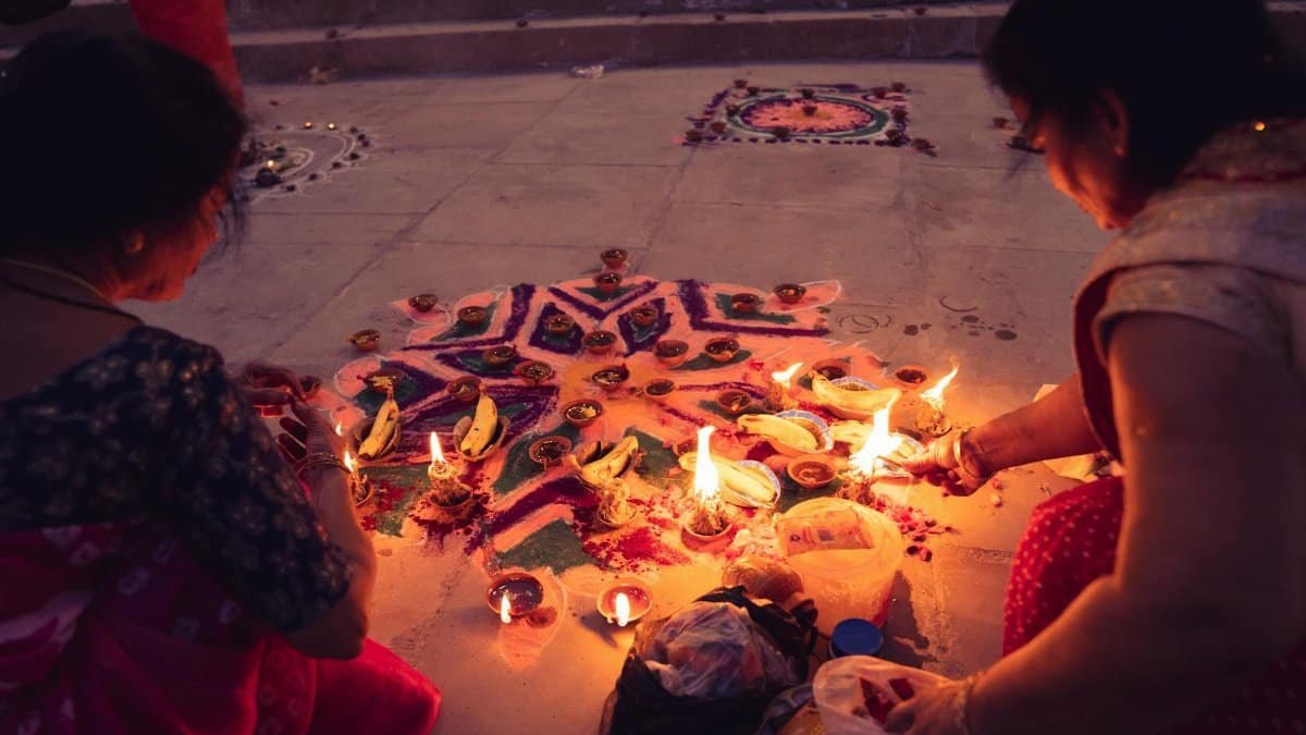 Two women creating a colorful rangoli with candles and flowers during a festival celebration.