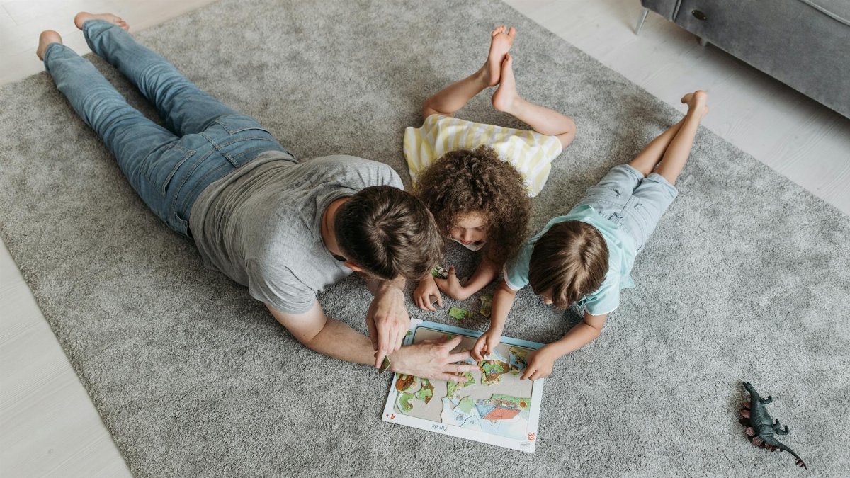 Father and kids enjoy quality time solving a puzzle together on a living room rug.