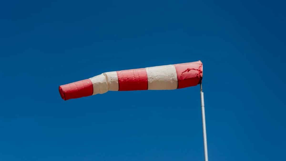 Vibrant red and white windsock blown by the wind against a clear blue sky.